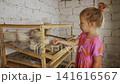 Curious little girl carefully feeding white quails from her hand through the bars of a wooden cage at a domestic poultry farm, fostering a connection between child and animal. 141616567