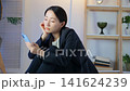 A middle-aged woman is troubled, looking at her smartphone in a dark room. Feeling down, looking at social media and videos, feeling lonely, sad, depressed, anxious, worried. 141624239