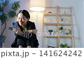A middle-aged woman looking at her smartphone in a dark room. Staying up late, late at night, videos, social media, smiling, chatting, romance, loneliness, single. 141624242
