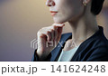 A middle-aged woman contemplates in a darkened room. Serious thoughts, doubts, business owner, manager, decision, choice, worries, anxiety, concern, job change, dissatisfaction. 141624248