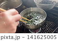 Blanching wakame seaweed in a small pot of boiling water. 141625005