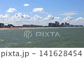 Coastal City Skyline and Wide Sandy Beach with Sea Waves on a Sunny Day, Perfect for Travel and Vacation Concepts 141628454