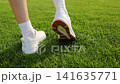 Female athlete applies medical adhesive bandage to a heel blister caused by uncomfortable footwear after sports training on a football stadium. Foot care, friction protection, injury prevention 141635771