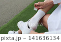 Female athlete applies adhesive bandage to a heel blister and puts on a sports sock while sitting on a bench at a football stadium. Close up of foot care, blister protection, injury prevention, sports 141636134