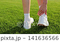 Female athlete removes sneaker and sock to check a heel blister after sports training on a football stadium field. Close up of foot discomfort from intensive exercise, uncomfortable footwear, injury 141636566