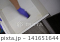 Person hand wearing blue rubber glove scrubs white kitchen drawer interior with black sponge removing dirt and stains during household cleaning process 141651644