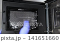Person hand in blue protective glove cleaning inside of black microwave oven with sponge and foamy detergent solution during domestic chore 141651660