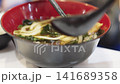 Close-up of chopsticks lifting thick udon noodles and seaweed from a bowl of hot Japanese soup. Professional food photography highlighting traditional Asian cuisine and authentic dining experience. 141689358