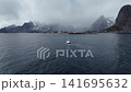 Small fishing boat crossing choppy northern coastal waters toward snow-dusted rocky mountains 141695632