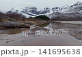 Rocky low-tide shoreline with reflective tidal pools and snow-capped mountains 141695638