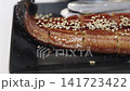 Close-up of grilled Japanese unagi eel topped with toasted white sesame seeds and a sweet soy glaze. Traditional kabayaki style eel served on a dark plate. Shallow depth of field focus. 141723422