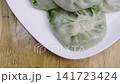 Top view close-up of steamed Chinese chive dumplings on a white plate. Thin translucent skin reveals fresh green vegetable filling. Traditional Asian dim sum appetizer. Healthy food photography style. 141723424
