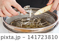 A woman's hands as she slices burdock root with a peeler. 141723810