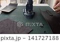 Artisan craftsman installing metal rivets on genuine leather using a hand press machine in a workshop 141727188