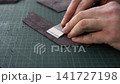 Leather craftsman scraping suede with a special knife for making handmade products on a cutting mat in a workshop 141727198
