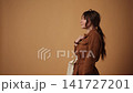 Pretty young woman posing with a white tote bag in a studio with a warm brown background and smiling at the camera 141727201