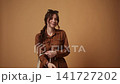 Stylish smiling woman with reusable tote bag dancing and having fun in a studio against a brown background 141727202