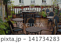 Quiet outdoor cafe terrace with wooden deck, round tables, woven chairs, and potted greenery 141734283