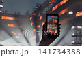Hand holding smartphone recording live concert stage with bright orange lights and crowd atmosphere 141734388