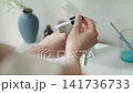 A woman pours serum onto her hand. 141736733
