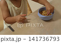 テーブルでボウルからシリアルをつまんで食べる子供の手元 141736793