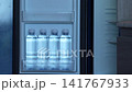 Little girl in a red dress taking a bottle of drinking water from an opened hotel room mini refrigerator highlighting family travel, child independence, and complimentary in room amenities. 141767933