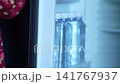 Little girl in a red dress taking a bottle of drinking water from an opened hotel room mini refrigerator highlighting family travel, child independence, and complimentary in room amenities. 141767937