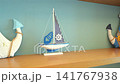 Decorative white anchor and miniature sailboat displayed on a wooden shelf against a soft blue background. Minimal coastal styling creates a clean maritime interior. 141767938