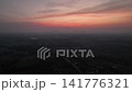Aerial footage rural village in Nong Bua Lamphu nestled in nature under a vibrant orange sunset sky. Street lights and houses begin to illuminate as dusk transitions into night. 141776321