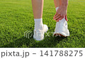Female athlete takes off sneaker and sock to inspect a heel blister after sports training on a football stadium field. Close up of foot discomfort from intensive exercise, improper footwear, injury 141788275