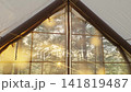 Cozy tent interior with quilted sleeping pad, mesh window, sunrise over pine forest, warm golden light filtering through fabric walls and soft morning shadows across camp bed 141819487