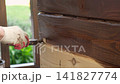 Brown oil for protection of wood by staining. Painting fence for protecting and pests. Woodworker applying finish to pine board box. Repairman varnishing with brush wooden fencing wall plank surface. 141827774