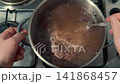 Person stirring beef shank in a pot of boiling broth 141868457