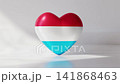 A heart shape appears in red, white, and blue colors. The design represents the national colors of Luxembourg. The heart sits on a flat surface with light casting shadows around it 141868463