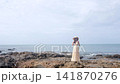 Young Asian Woman in Maxi Dress and Straw Hat Standing on Rocky Ocean Shore in Lanta Island 141870276