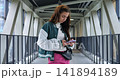 Indoor bridge crossing detail. Individual walking across bridge indoors with mobile device and bag. Person confidently steps across indoor bridge while focusing on phone and carrying pouch 141894189