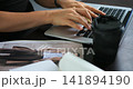 Laptop and coffee on table. Focused scene of hands typing email with coffee and magazine. Close detail of hands composing electronic message on keyboard alongside coffee and reading material 141894190