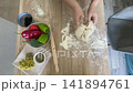 The hands of a female cook knead a lump of dough on a wooden table with white wheat flour. 141894761