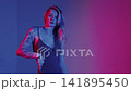 A blonde with a beautiful figure poses in a black bodysuit in a studio. Studio lighting, low exposure, neon. 141895450