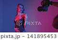 A blonde with a beautiful figure poses in a black bodysuit in a studio. Studio lighting, low exposure, neon. 141895453
