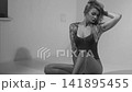 Blonde with a beautiful figure in a black bodysuit poses in the studio. Studio lighting, low exposure, monochrome light. 141895455