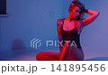 A blonde with a beautiful figure poses in a black bodysuit in a studio. Studio lighting, low exposure, neon. 141895456
