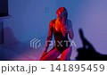 A blonde with a beautiful figure poses in a black bodysuit in a studio. Studio lighting, low exposure, neon. 141895459