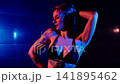 Seductive photo model takes a shower in a swimsuit, poses for a photographer. Studio lighting, blue and red light falls on the woman's body. 141895462