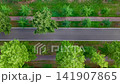 op-down drone video follows blue car driving along straight asphalt road bordered by lush green trees and park paths. Smooth aerial motion highlights transport, summer greenery and urban geometry 141907865