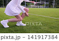 Sofia, Bulgaria - 7.22.26. Woman in white tennis outfit collecting a racket and ball on green sports field, recreational tennis training at outdoor stadium, active lifestyle and summer sport scene 141917384
