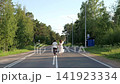 Rear view of two people running along double white centerline on rural road through dense birch and pine forest under clear daylight sky, with running, road, centerline, stride detail 141923334