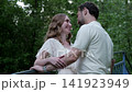 Affectionate pair leaning into near kiss on painted bridge in wooded park with soft backlight, relaxed smiles, gentle hold, and lush greenery surrounding scene, with embrace, kiss, affection 141923949