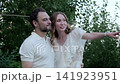 Adults sharing warm gestures and kisses in leafy garden, woman smiles and points while man leans close, then they hug and stand together in soft daylight, with garden, outdoors, adult, woman detail 141923951
