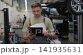 Mechanic man with clipboard walking along workshop. Car service, repair, maintenance and people. 141935631